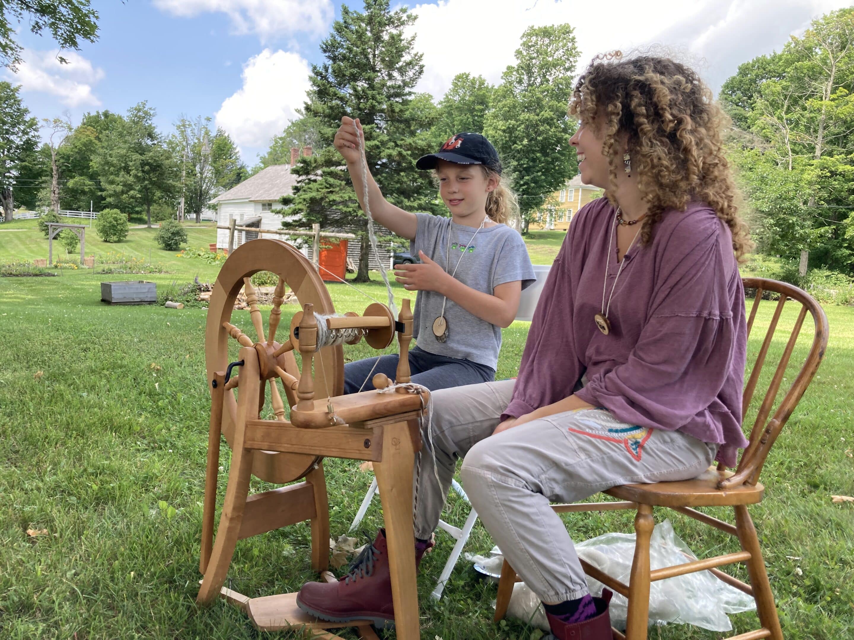 Two people sit next to a spinning wheel.